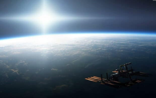 A space station orbits above Earth with the sun shining in the distance, HD Desktop Wallpaper