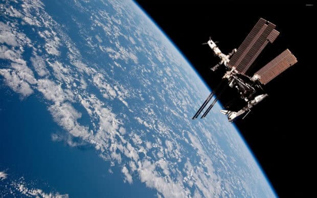 A space station orbiting above the cloud covered Earth in space, 2K Desktop Wallpaper