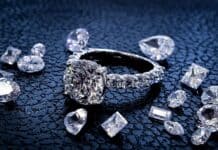 A sparkling diamond ring surrounded by various cut gems on a textured surface, HD Desktop Wallpaper