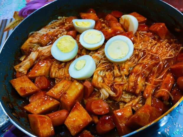 A pan filled with spicy enoki mushrooms, tofu cubes, sausages, and halved boiled eggs cooked in a rich sauce, HD Desktop Wallpaper