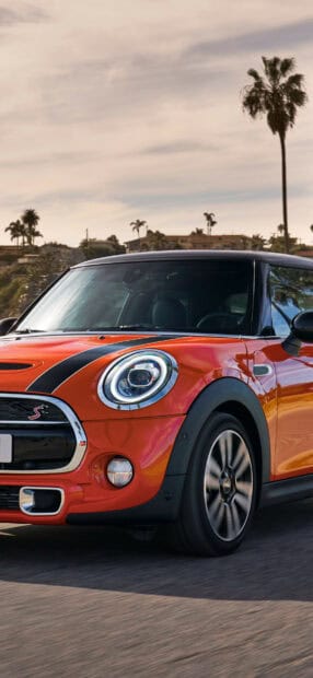 A red Mini Cooper is driving on the road with palm trees in the background, HD Mobile Wallpaper