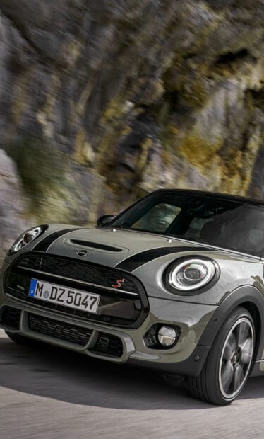 A Mini Cooper is seen speeding along a winding mountain road with rocky cliffs in the background, HD Mobile Wallpaper
