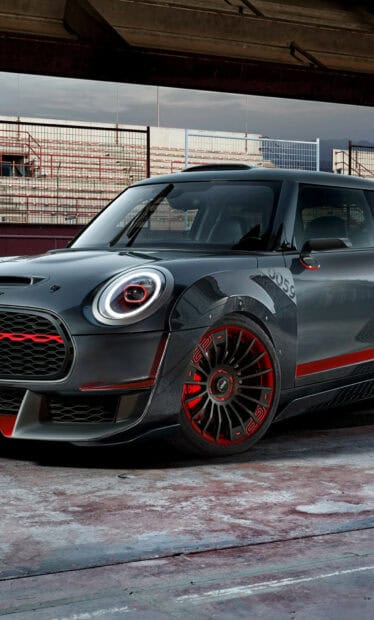 A black Mini Cooper with red accents is parked on a concrete surface near a stadium fence, HD Mobile Wallpaper