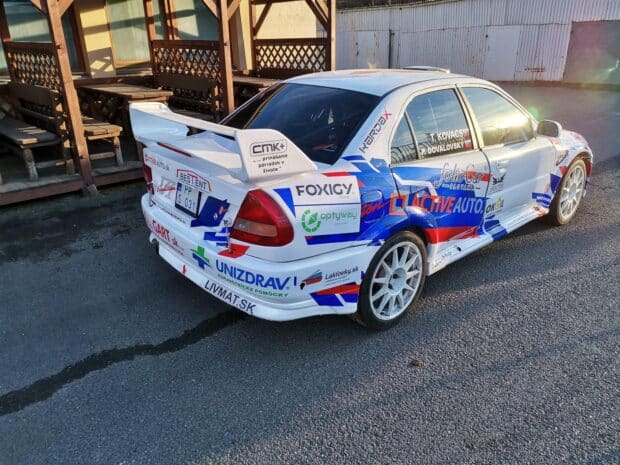 A white Mitsubishi Lancer Evo rally car with sponsor logos parked near wooden benches, HD Desktop Wallpaper