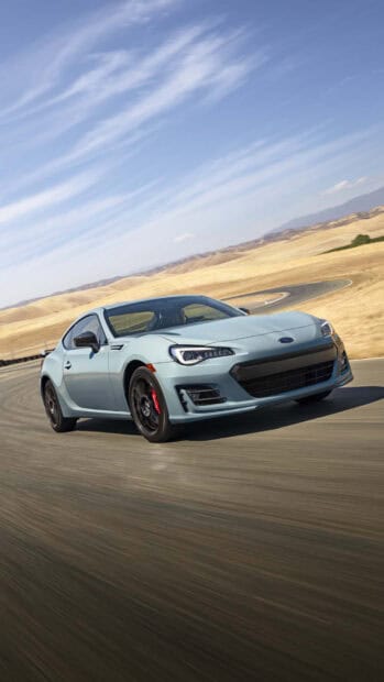 A sleek blue Subaru Brz is driving fast on a curvy road surrounded by dry hills under a clear sky, HD Phone Wallpaper