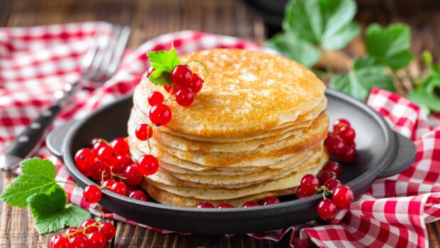 A stack of golden pancakes garnished with fresh red currants on a black skillet, 4K Desktop Wallpaper