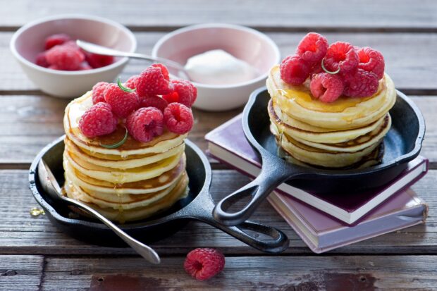 A stack of pancakes topped with fresh raspberries and drizzled with honey in cast iron pans, HD Desktop Wallpaper