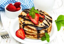 A stack of pancakes topped with fresh strawberries, chocolate syrup, and mint leaves on a white plate, 2K Desktop Wallpaper