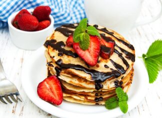A stack of pancakes topped with fresh strawberries, chocolate syrup, and mint leaves on a white plate, 2K Desktop Wallpaper