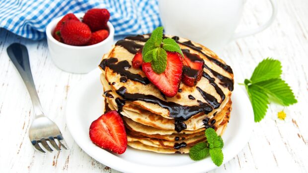 A stack of pancakes topped with fresh strawberries, chocolate syrup, and mint leaves on a white plate, 2K Desktop Wallpaper