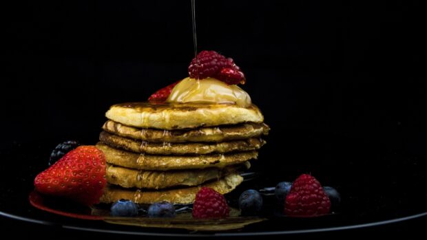 A stack of pancakes with syrup dripping and fresh berries around on a black plate, 4K Desktop Wallpaper