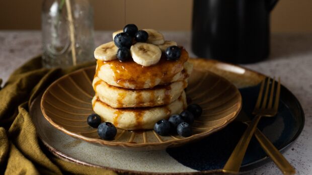 A stack of pancakes with blueberries and banana slices drizzled with syrup on a plate, 4K Desktop Wallpaper