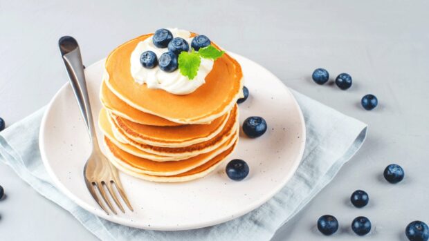 A stack of pancakes topped with whipped cream and fresh blueberries is served on a plate, HD Desktop Wallpaper