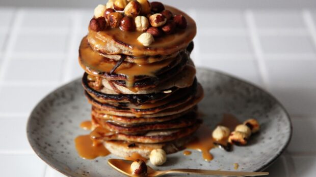 A stack of pancakes topped with caramel sauce and hazelnuts on a plate, 4K Desktop Wallpaper