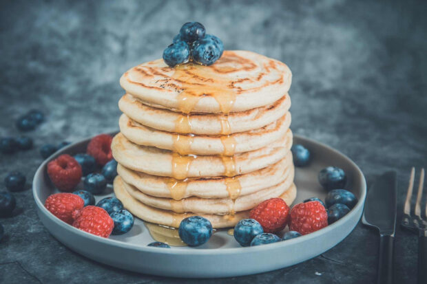 A stack of pancakes topped with blueberries and syrup surrounded by berries on a plate, HD Desktop Wallpaper