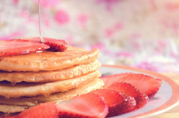 A stack of pancakes topped with sliced strawberries and syrup pouring over them, 2K Desktop Wallpaper