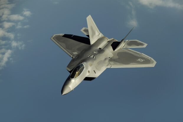 A stealth jet fighter is flying high against a blue sky with minimal clouds, 2K Desktop Wallpaper
