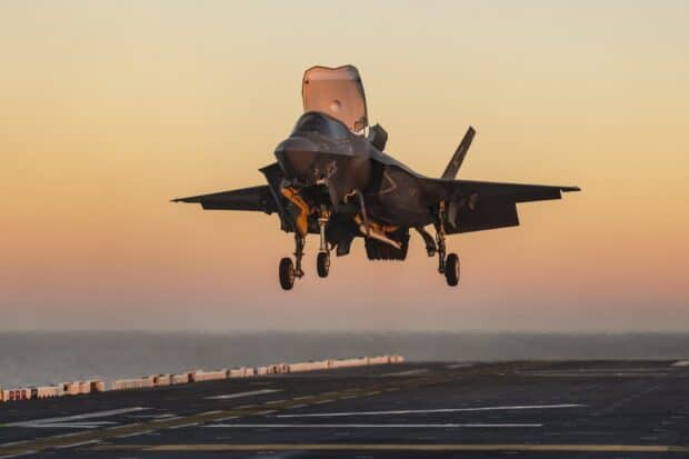A stealth jet fighter is landing on an aircraft carrier during sunset, HD Desktop Wallpaper