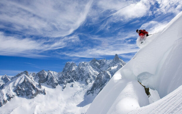 A skier is descending a steep snowy mountain surrounded by tall peaks under a blue sky, HD Desktop Wallpaper