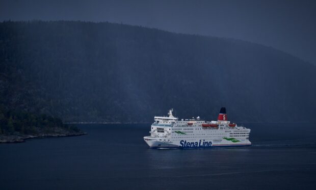 A Stena Line ferry sails calmly near the coast under a dark sky with forested hills, 2K Desktop Wallpaper