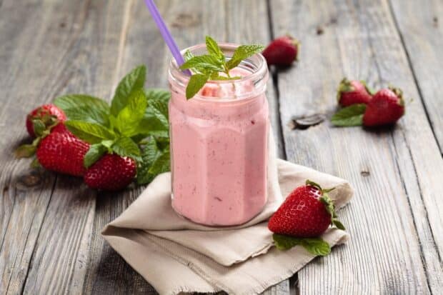 A jar of strawberry milkshake garnished with mint leaves and fresh strawberries on a wooden table, HD Desktop Wallpaper
