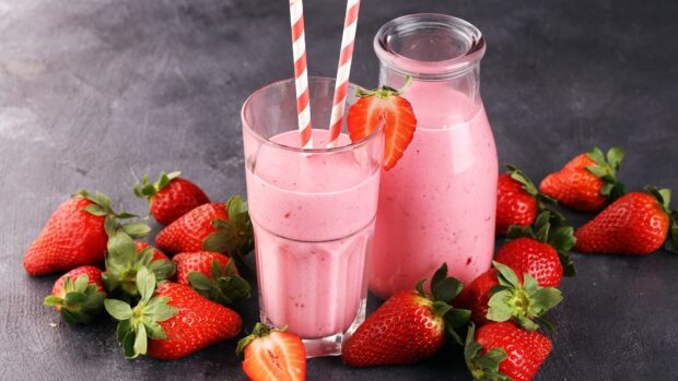 A glass and bottle of strawberry milkshake surrounded by fresh strawberries on a dark surface, HD Desktop Wallpaper