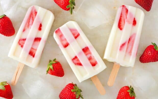 Three strawberry popsicles with fresh fruit slices and ice cubes on a surface, 2K Desktop Wallpaper