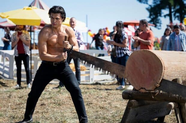 A muscular man uses a large saw to cut a wooden log during an outdoor event, HD Desktop Wallpaper