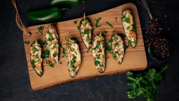 Stuffed jalapenos with cheese and herbs arranged on a wooden board for a delicious meal, 2K Desktop Wallpaper