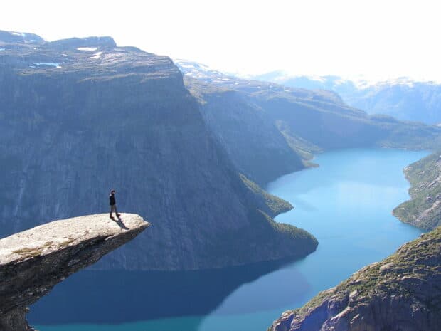 A person stands on a cliff overlooking the Norwegian fjords with clear blue water and mountains, HD Desktop Wallpaper