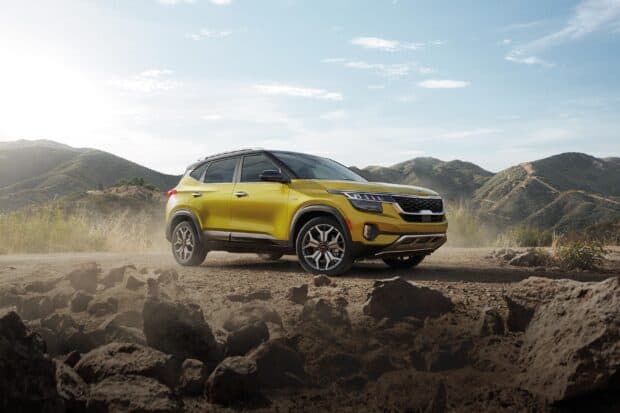 A yellow Kia SUV drives through rocky mountain terrain under a clear sky showcasing Kia Wallpapers, 2K Desktop Wallpaper