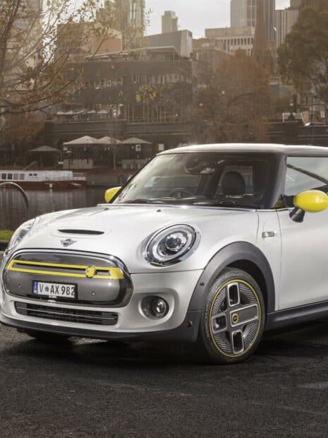 A white Mini Cooper with distinctive yellow details parked near a river in the city, HD Mobile Wallpaper