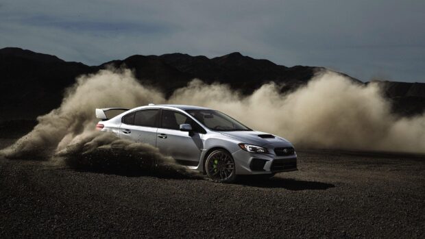 A Subaru Wrx is kicking up dust while drifting on a rugged dirt surface near mountains, HD Desktop Wallpaper
