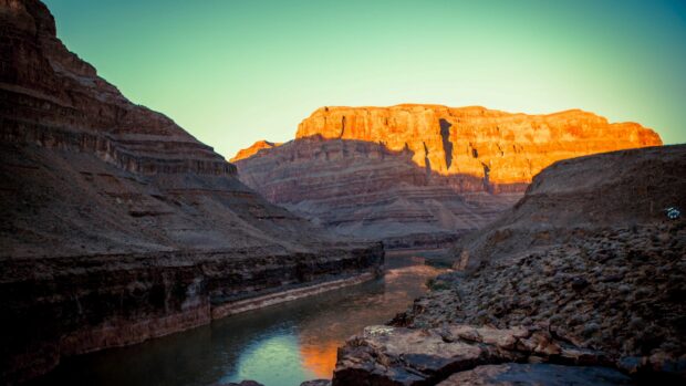 The Grand Canyon displays vibrant rock formations glowing in sunlight near a winding river, 4K Desktop Wallpaper