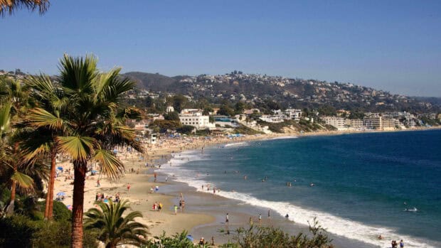 The Laguna Beach coastline shows sandy shores with people enjoying the sea and sun, 4K Desktop Wallpaper