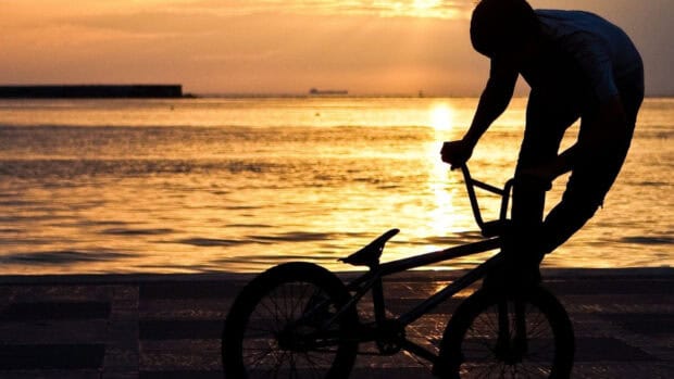 A BMX rider performs a trick by the ocean at sunset showcasing BMX sports, HD Desktop Wallpaper