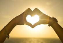 Hands forming a heart shape with sunset over the ocean, 2K Desktop Wallpaper