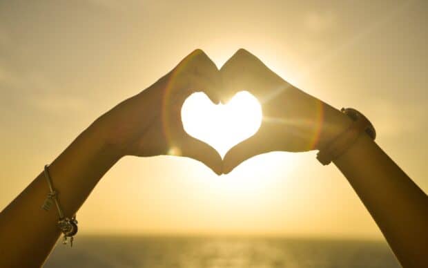 Hands forming a heart shape with sunset over the ocean, 2K Desktop Wallpaper