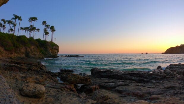 The waves crash against rocky cliffs at Laguna Beach during sunset, 4K Desktop Wallpaper