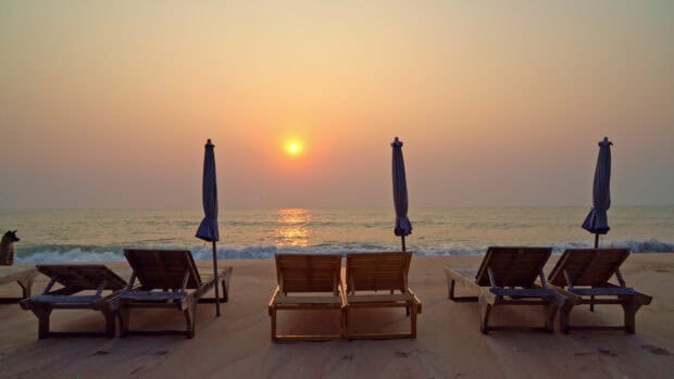 The sunset shines over calm sea with beach umbrellas and chairs, 4K Desktop Wallpaper