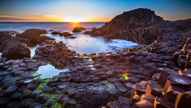 A breathtaking view of the Giant's Causeway coastline during sunset with hexagonal basalt columns and calm sea, HD Desktop Wallpaper