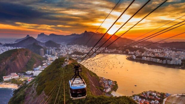 A cable car rides over the hills and bay with Rio De Janerio city in the background at sunset, 4K Desktop Wallpaper