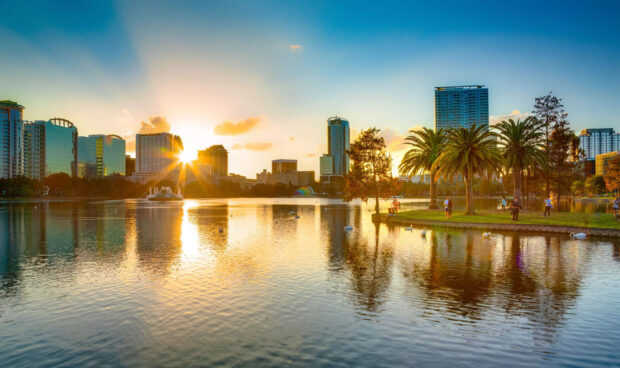 The calm lake reflects the Orlando skyline at sunset with palm trees and people relaxing nearby, 2K Desktop Wallpaper