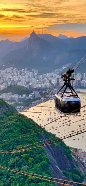 A cable car rides above the lush green hills overlooking Rio de Janeiro with the Christ the Redeemer statue in the background, 2K Phone Wallpaper
