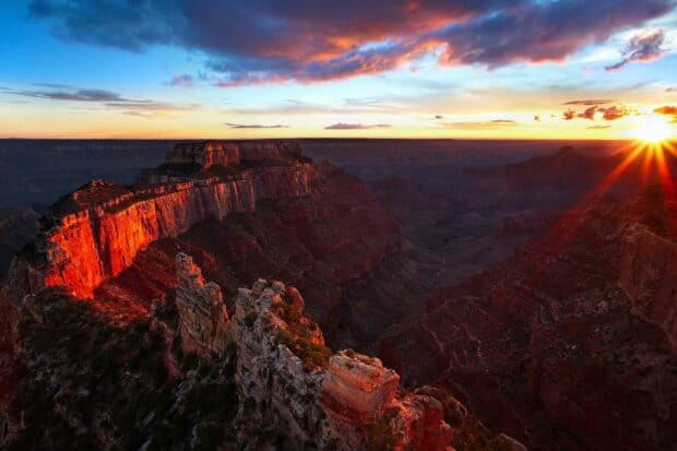 The sun sets behind the rocky Grand Canyon illuminating the cliffs with warm light, HD Desktop Wallpaper