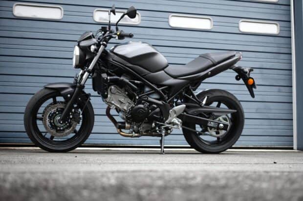 A matte black Suzuki Sv650 motorcycle parked in front of a gray garage door, HD Desktop Wallpaper