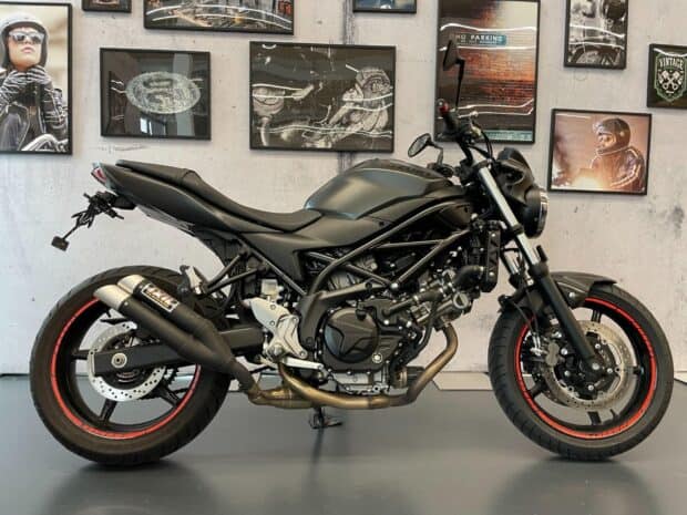 A matte black Suzuki Sv650 motorcycle is displayed against a wall with framed pictures, HD Desktop Wallpaper