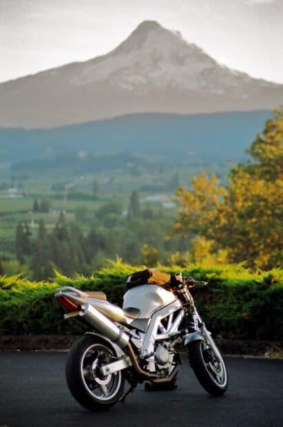 A Suzuki Sv650 is parked on a road with a mountain and green landscape in the background, 2K Mobile Wallpaper