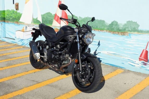 A Suzuki Sv650 motorcycle is parked on a street with a colorful waterfront mural in the background, HD Desktop Wallpaper