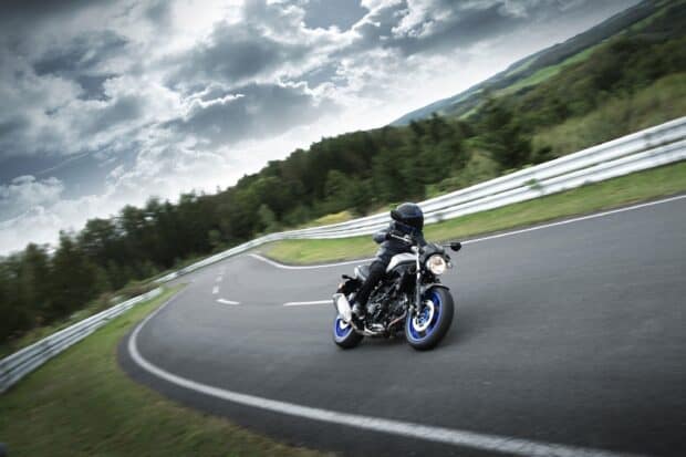 A person rides a Suzuki Sv650 on a winding mountain road under a cloudy sky, 2K Desktop Wallpaper